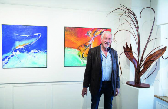 Jean-Daniel Cart pose devant ses peintures à l’huile et à côté de sa sculpture le bouquet en écorce de sapin. PHOTOS RÉGINE GAPANY