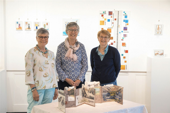 Trois des cinq membres d’Art-tex (de gauche à droite, Patricia Fuentes, Marianne Bender et Martine Mercier) posent devant le livre montagne de la Valaisanne au centre. RÉGINE GAPANY