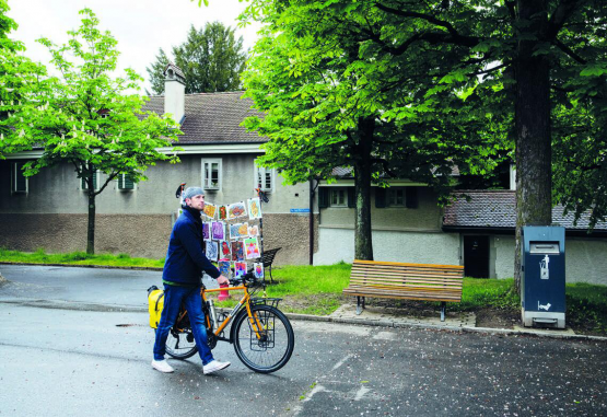 A la galerie Trait Noir, Lucien Pilloud affiche ses œuvres et son iconique vélo avec ses cartes postales installées dessus. CÉLINE GRANGER